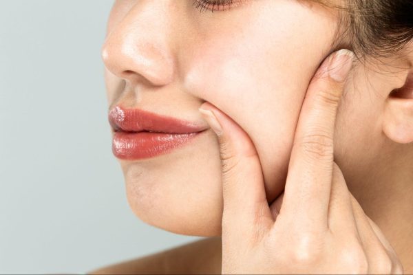 頬のたるみが気になり、頬をつまんでいる女性