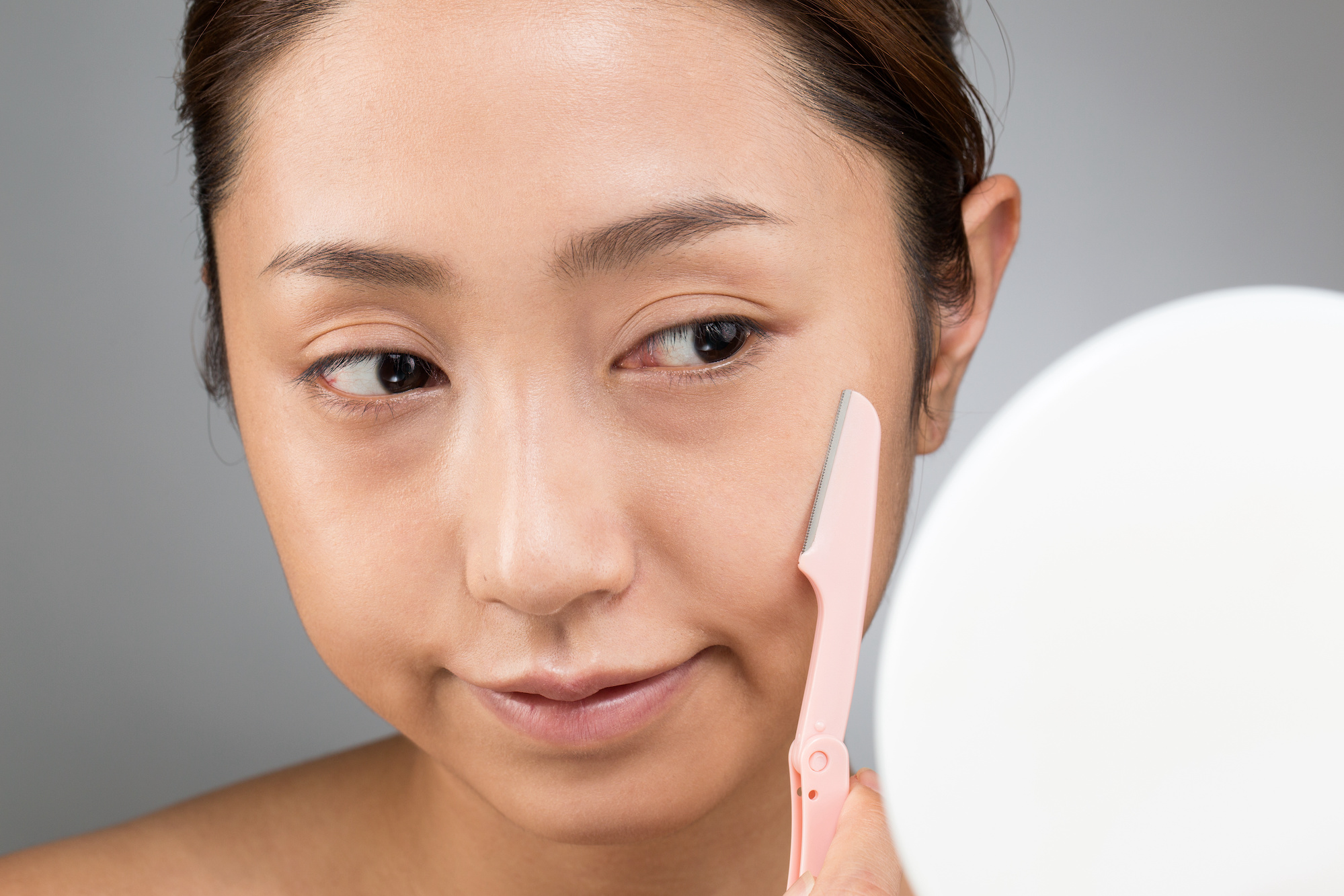 顔にカミソリをあてる女性