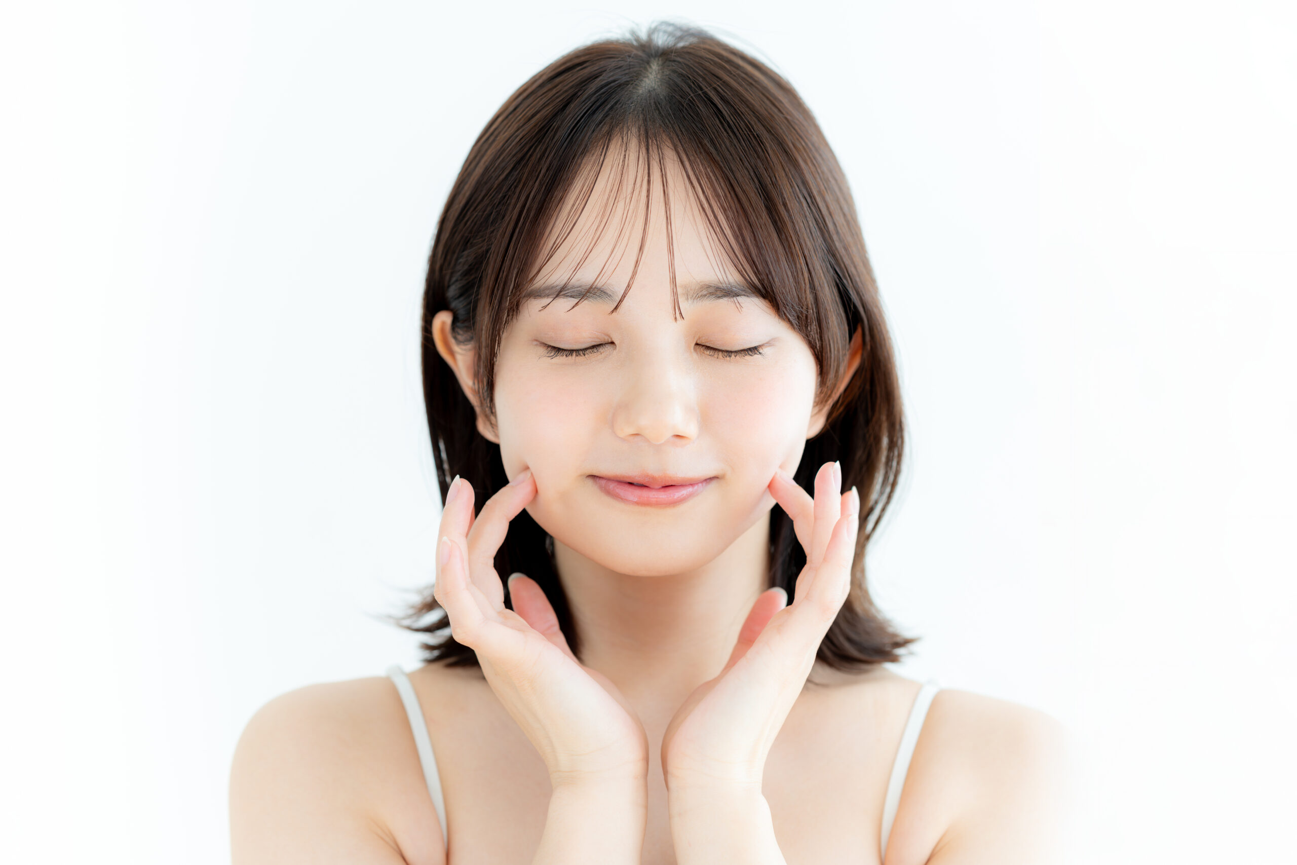 目を閉じて、両手で頬に触れている女性